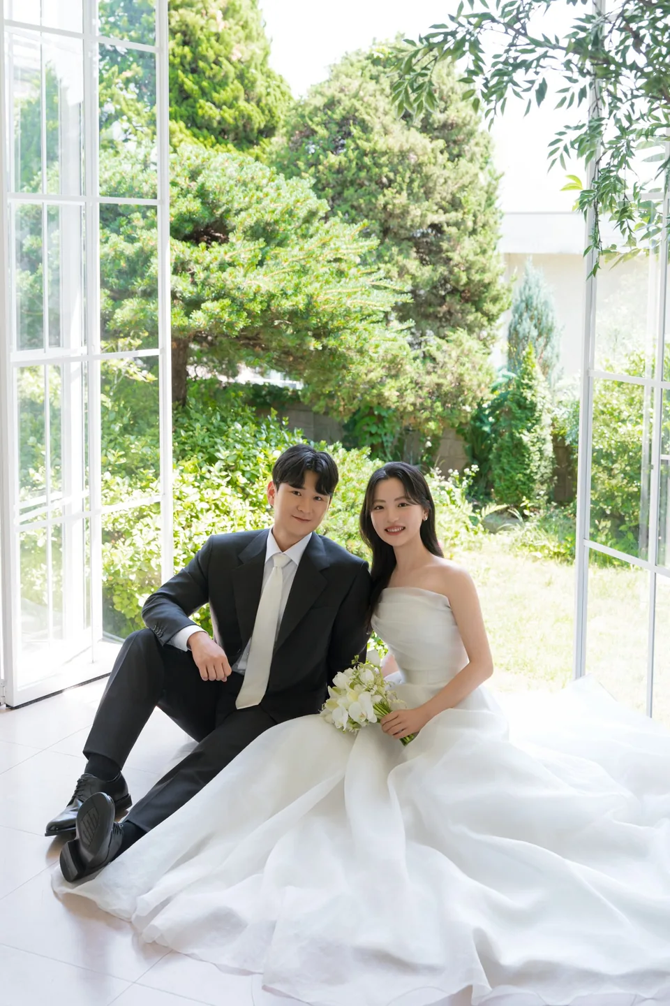초록 나무가 보이는 창가에 앉아 나란히 웃는 상우와 지윤